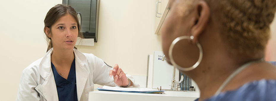 A healthcare provider sits while talking to another sitting person in a clinic